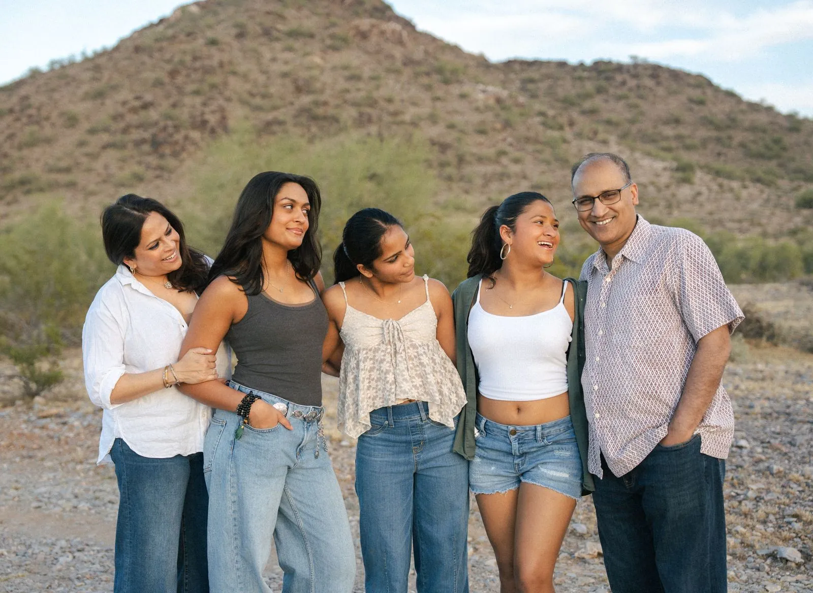 Family of five in soft neutral colours laughing in front of a desert mountain