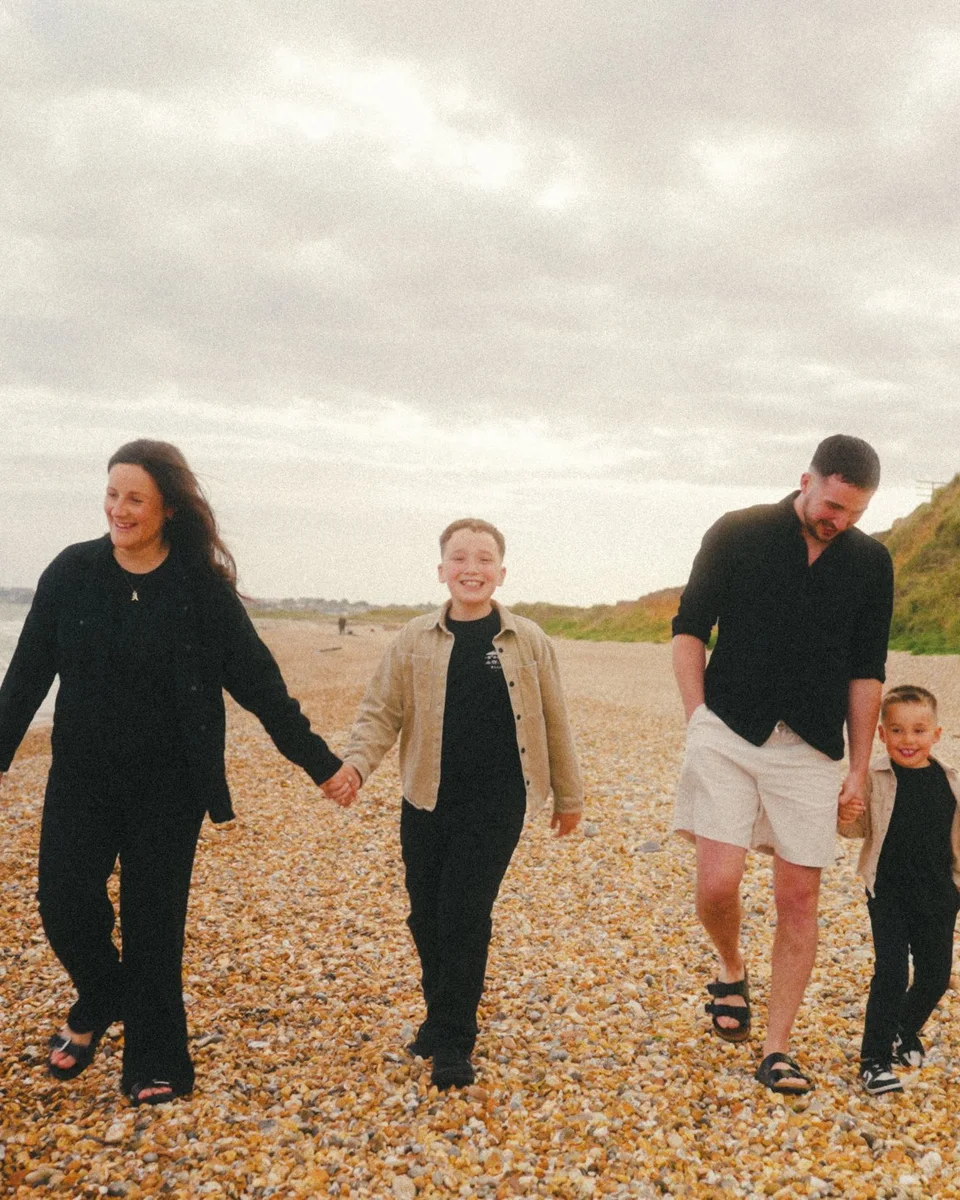 Family of four walking hand in hand along a pebble beach
