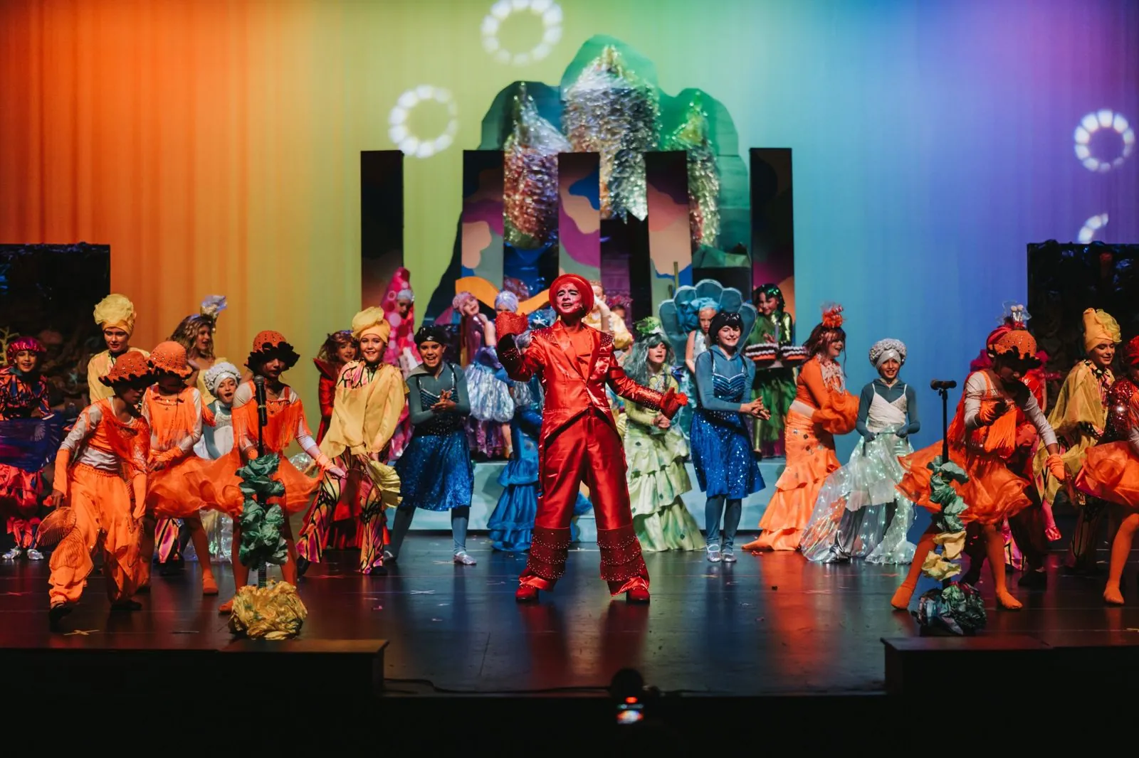 Full youth theatre cast on a brightly lit stage during a musical
